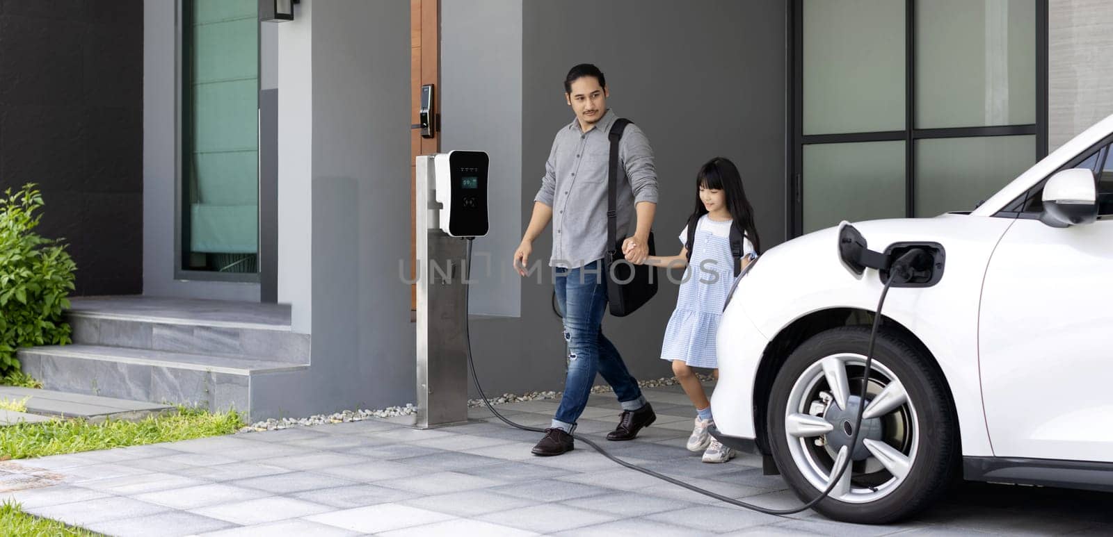 Progressive dad and daughter charging EV car from home charging station. by biancoblue