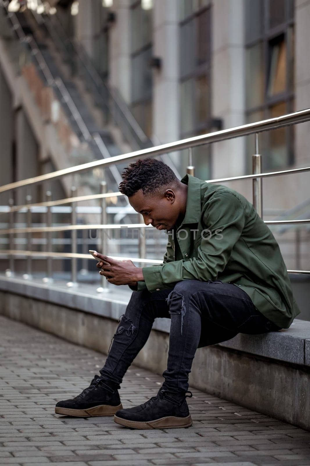 young african american man in jacket messaging online, checking social networks outdoor
