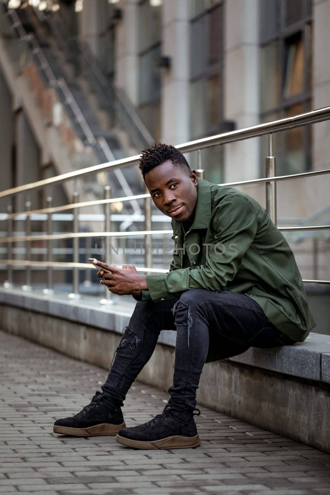 young african american man in jacket messaging online, checking social networks outdoor