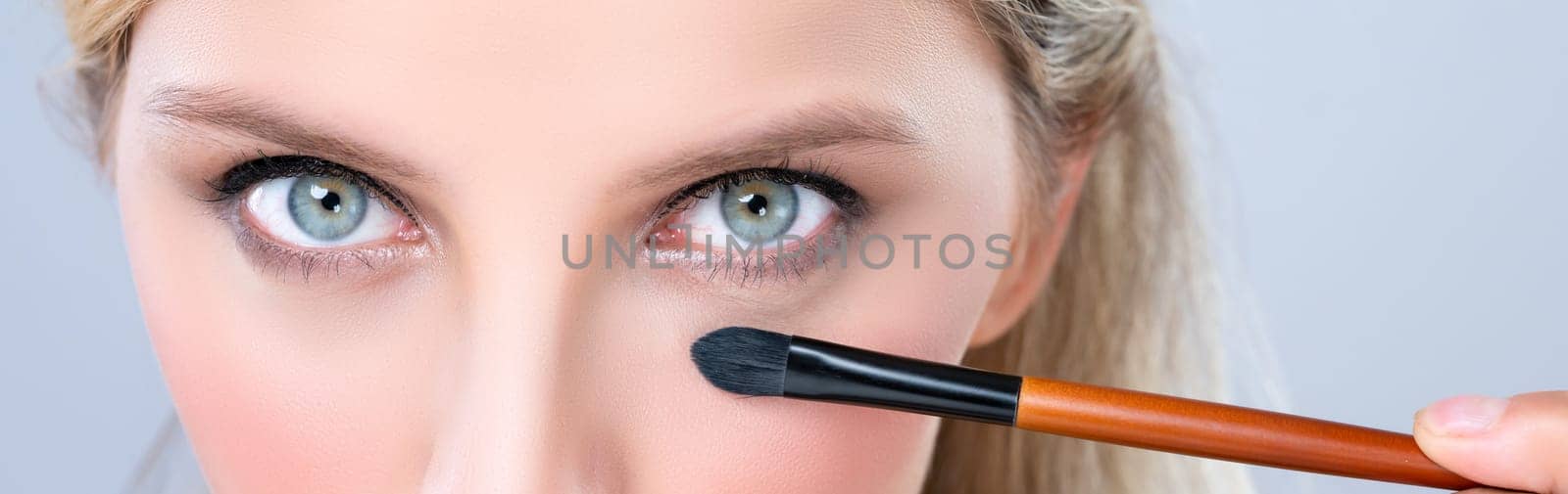 Closeup beautiful girl with flawless applying alluring eye shadow makeup with eyeliner brush. Cosmetic facial painting process on lovely young woman with perfect clean skin on isolated background.