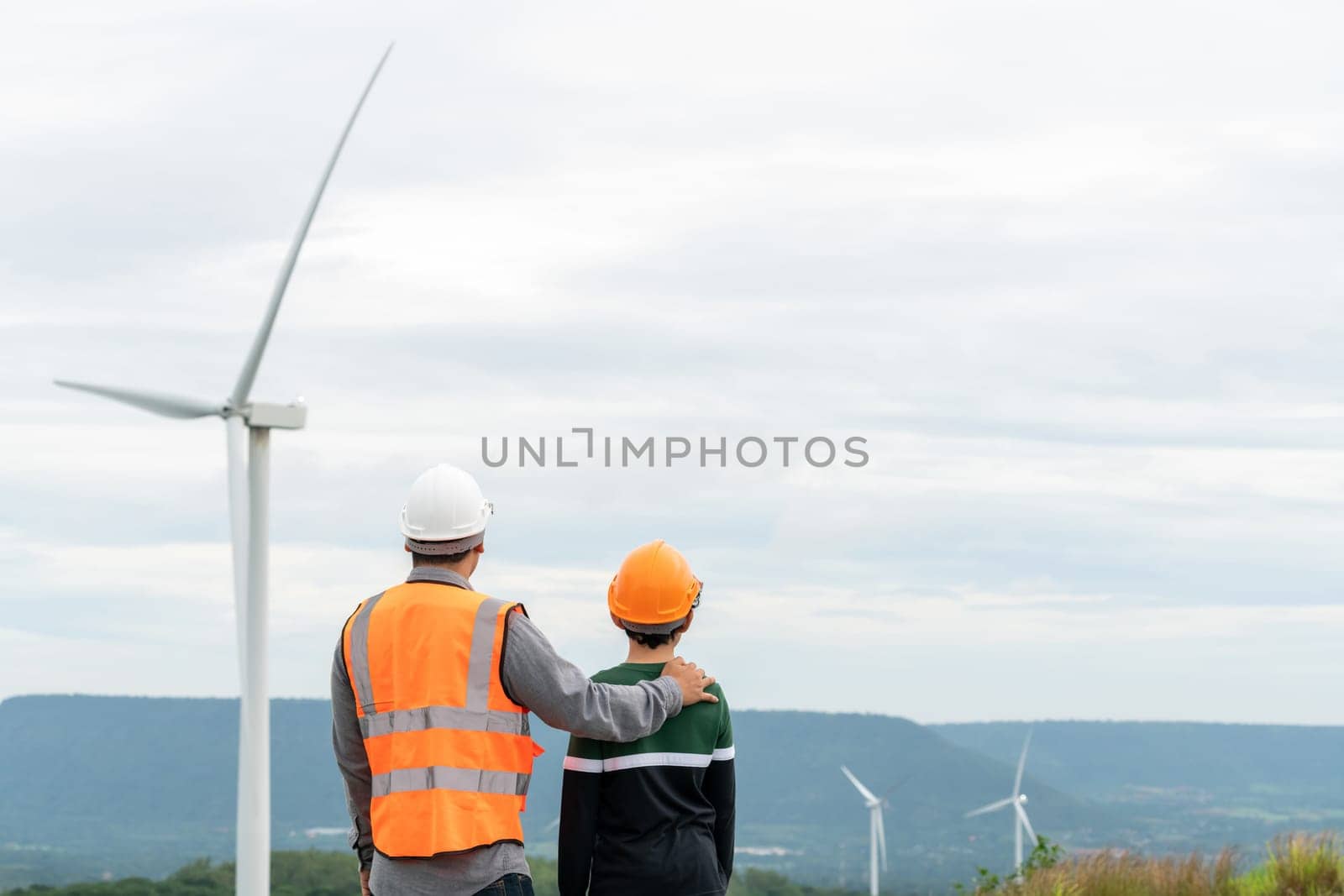 Engineer with his son on a wind farm atop a hill or mountain in the rural. Progressive ideal for the future production of renewable, sustainable energy. Energy generation from wind turbine.