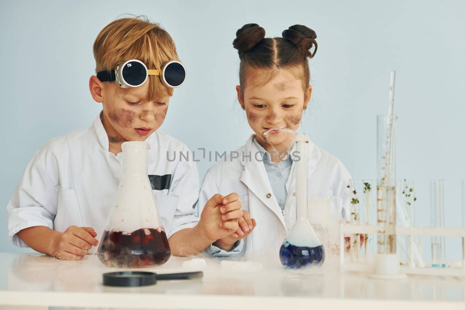 Boy works with liquid in test tubes. Children in white coats plays a scientists in lab by using equipment.