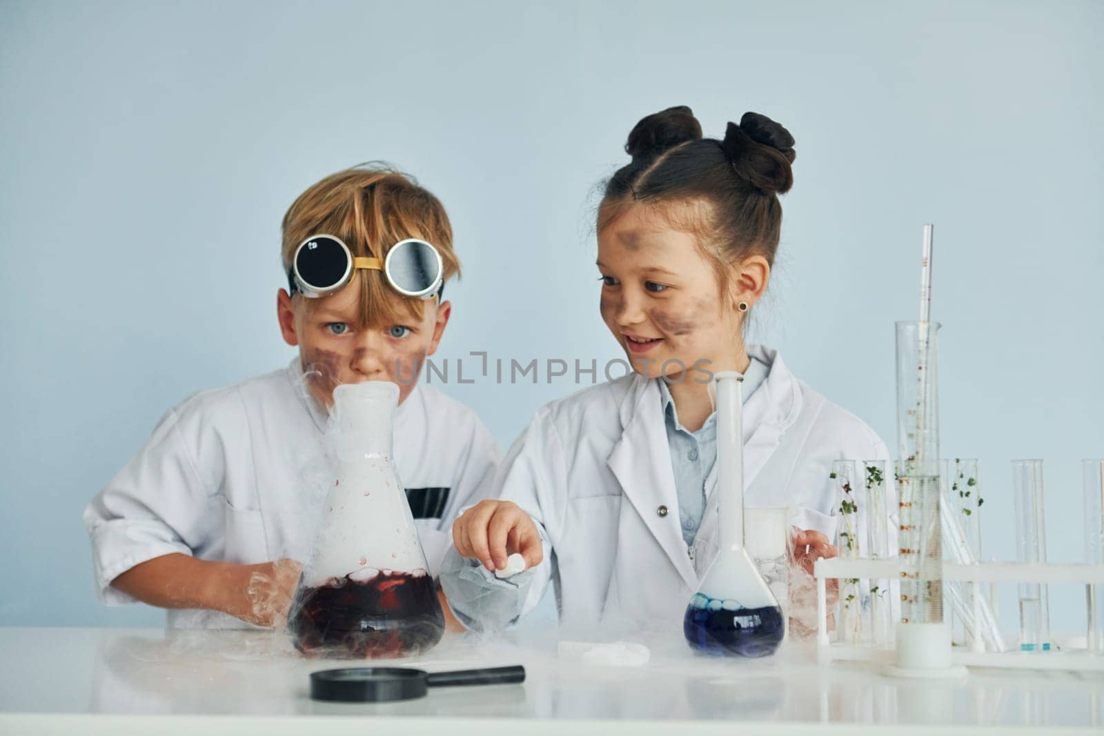 Boy works with liquid in test tubes. Children in white coats plays a scientists in lab by using equipment by Standret