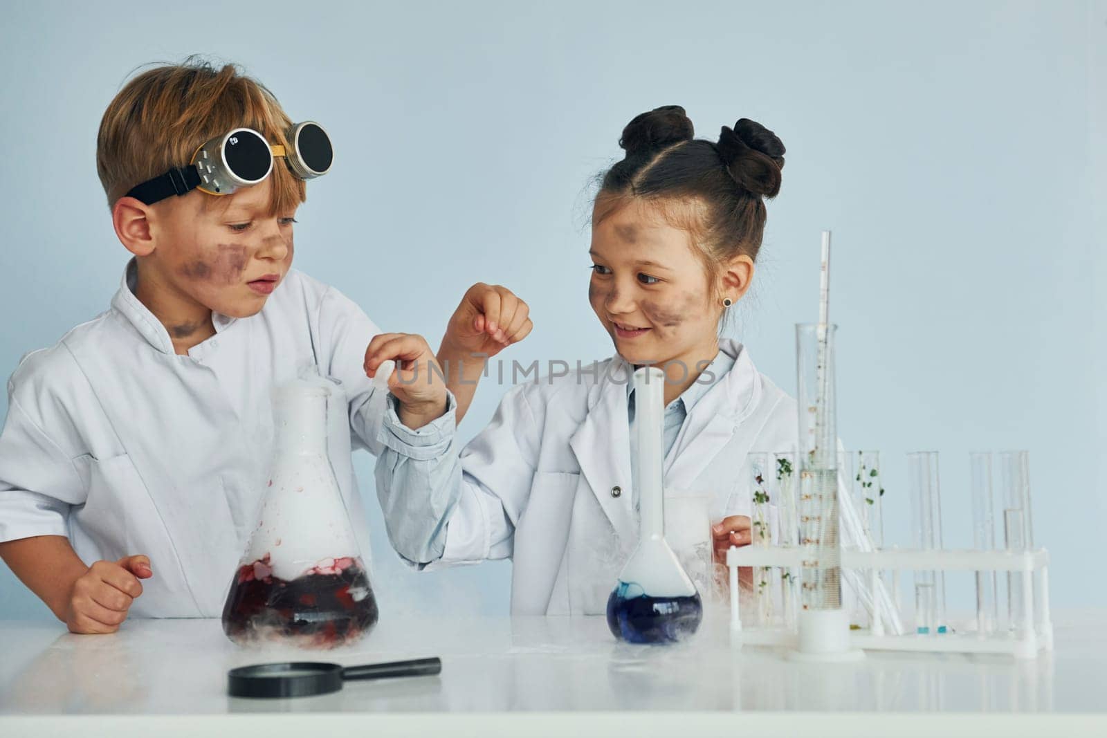 Boy works with liquid in test tubes. Children in white coats plays a scientists in lab by using equipment by Standret