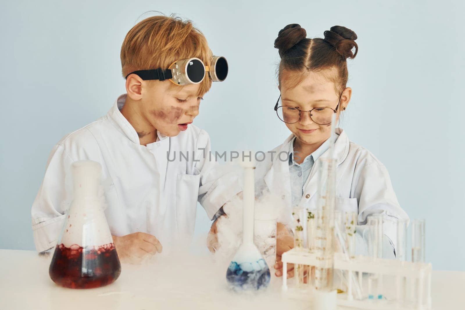 Girl with boy working together. Children in white coats plays a scientists in lab by using equipment.