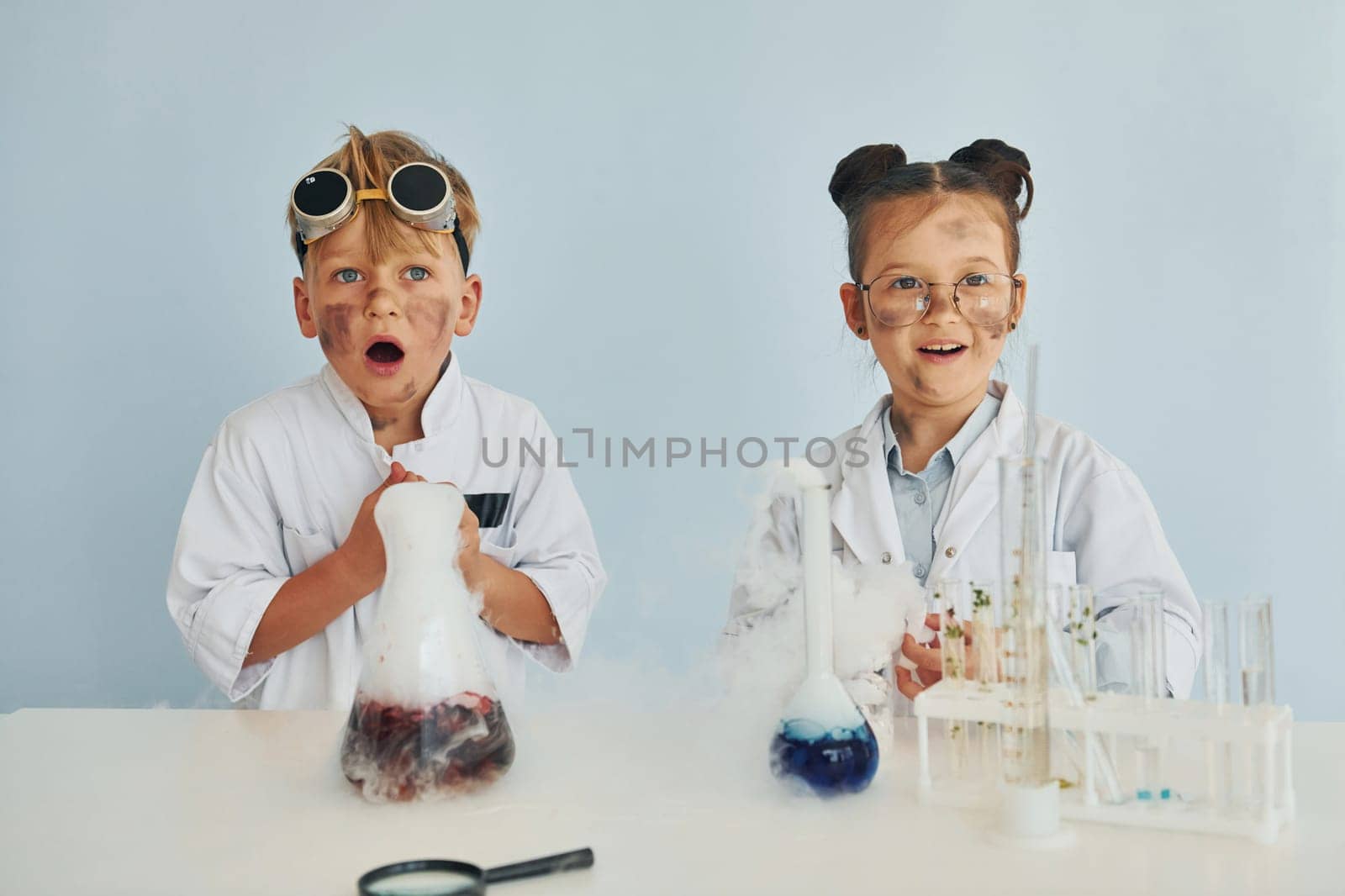 Girl with boy working together. Children in white coats plays a scientists in lab by using equipment.