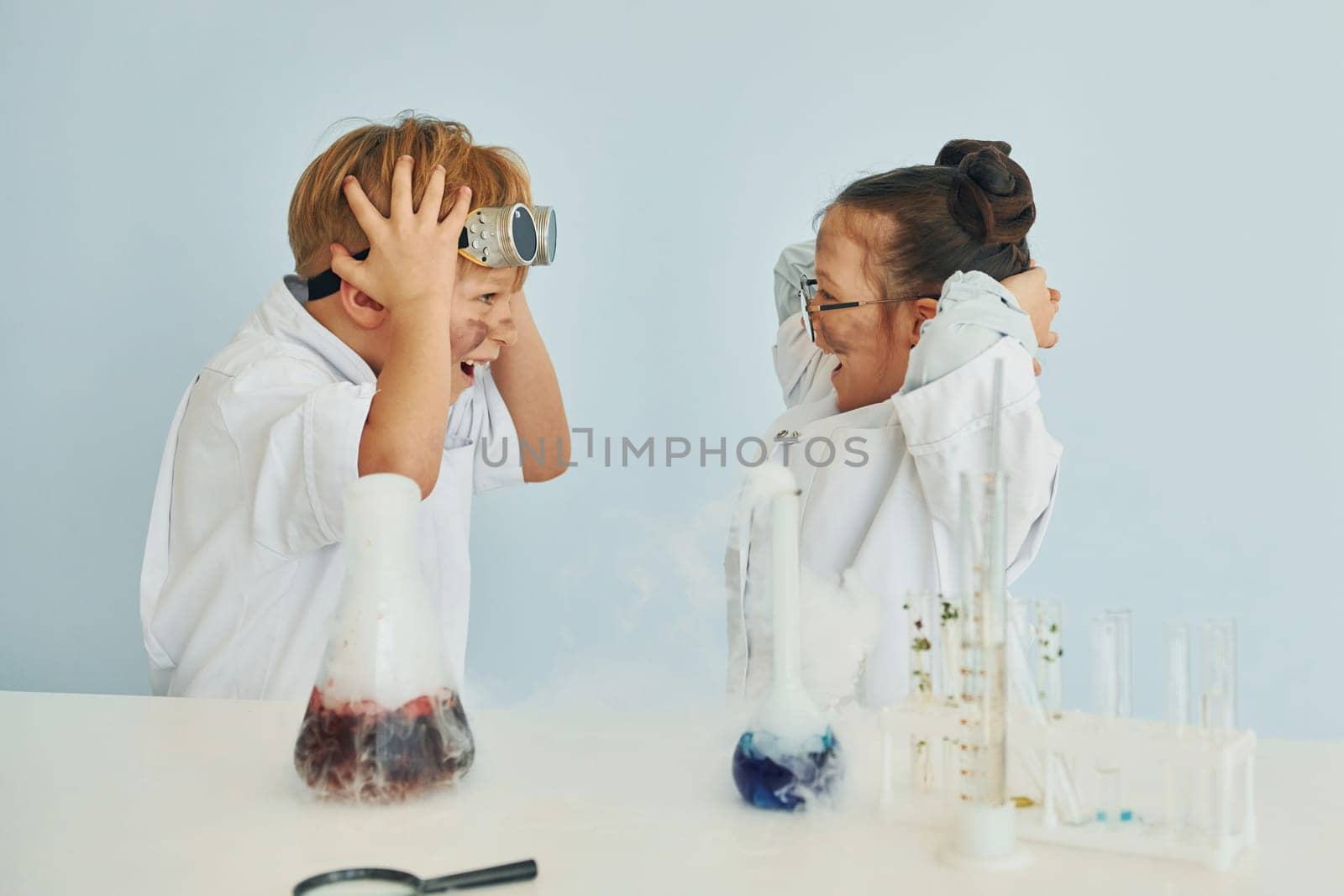 Girl with boy working together. Children in white coats plays a scientists in lab by using equipment by Standret
