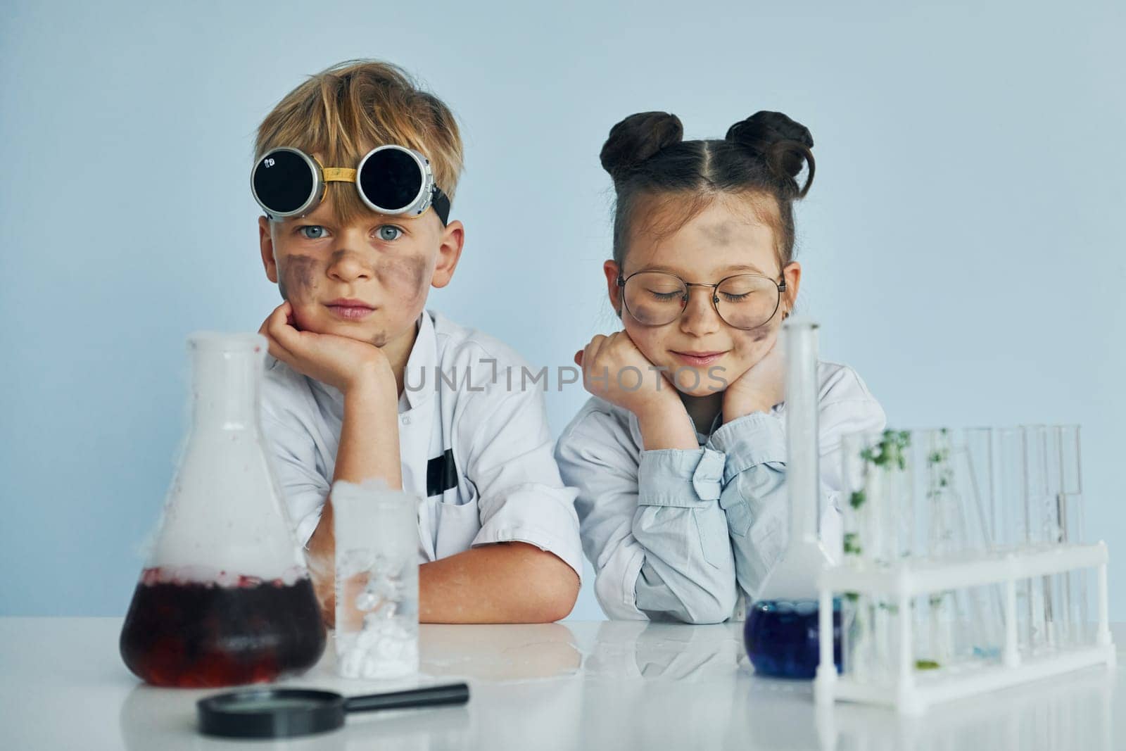 Girl with boy working together. Children in white coats plays a scientists in lab by using equipment by Standret