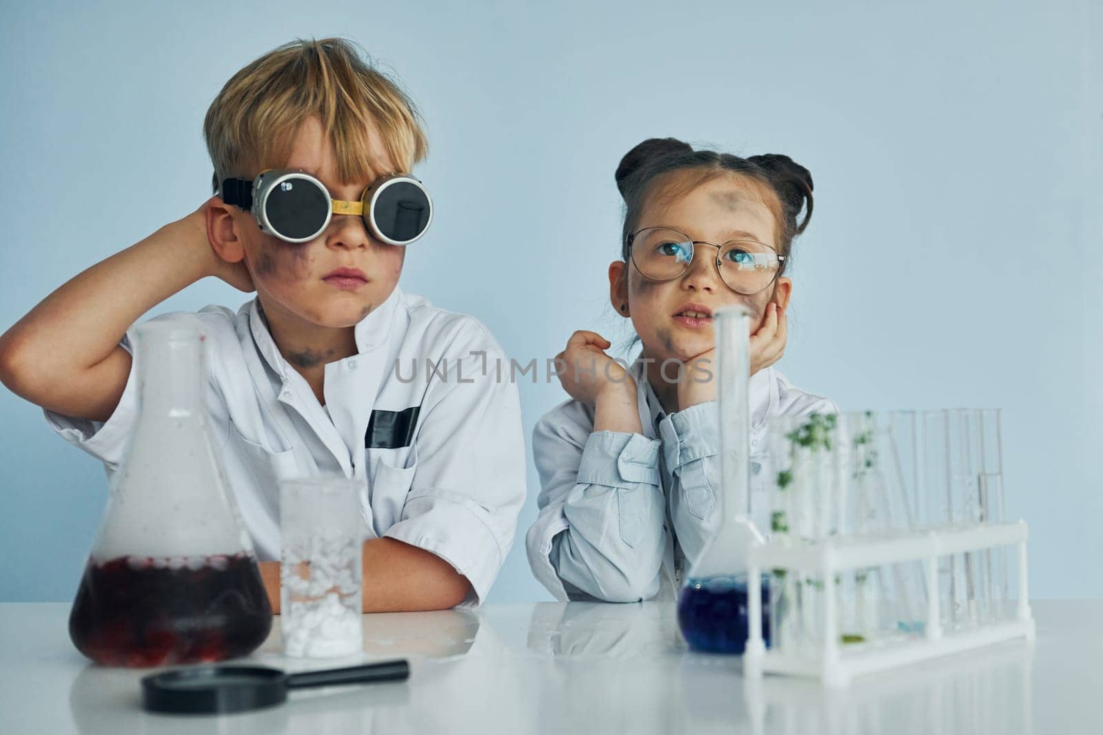 Girl with boy working together. Children in white coats plays a scientists in lab by using equipment by Standret