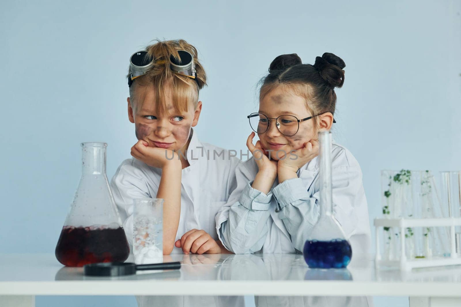 Girl with boy working together. Children in white coats plays a scientists in lab by using equipment.