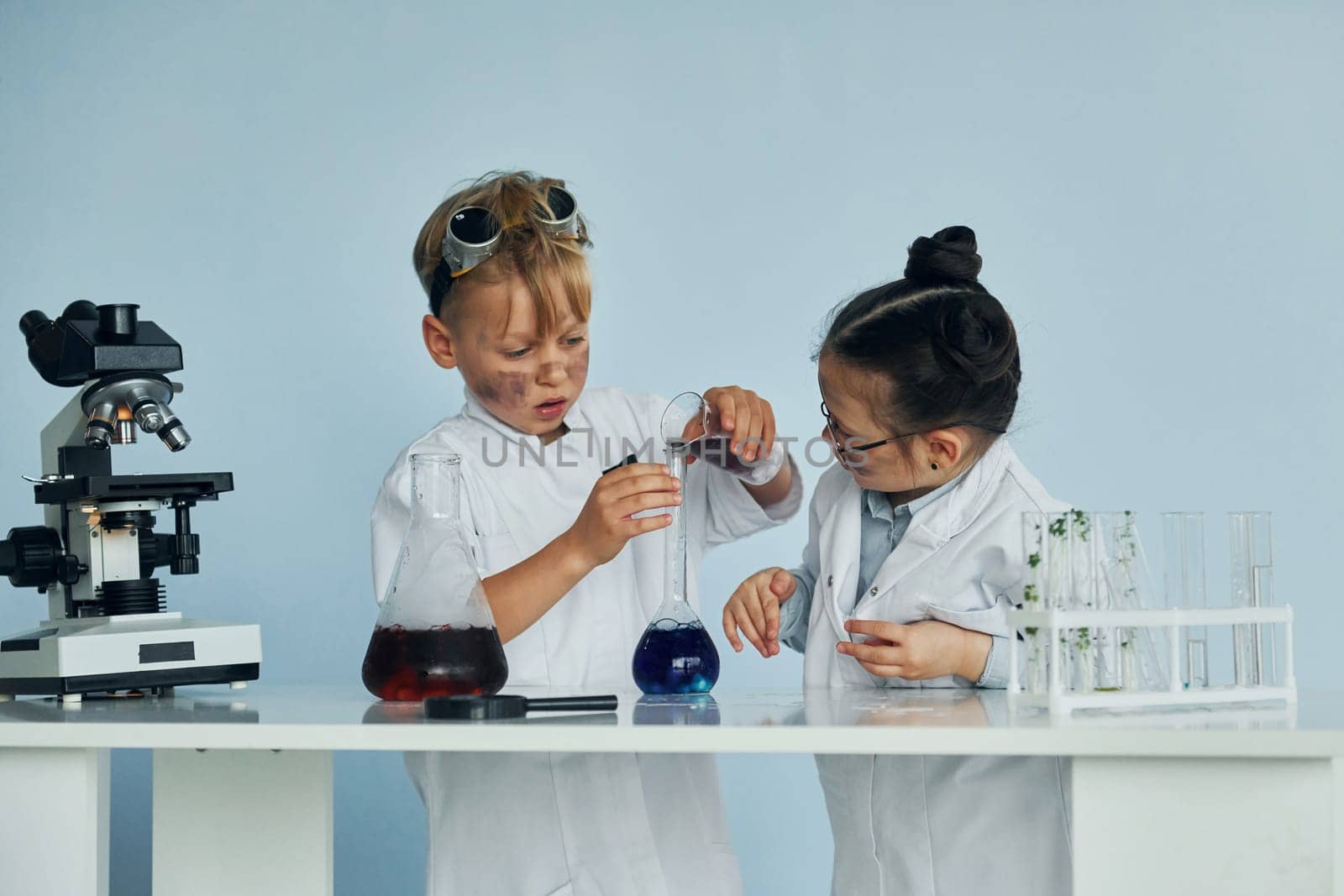 Little girl and boy in white coats plays a scientists in lab by using equipment by Standret