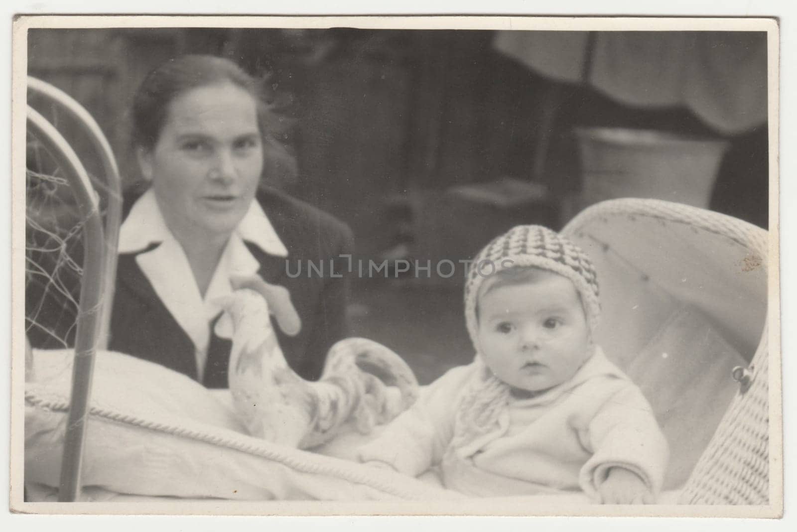 Vintage photo shows mother and her baby sits in the pram - carriage. Retro black and white photography. Circa 1970s. by roman_nerud