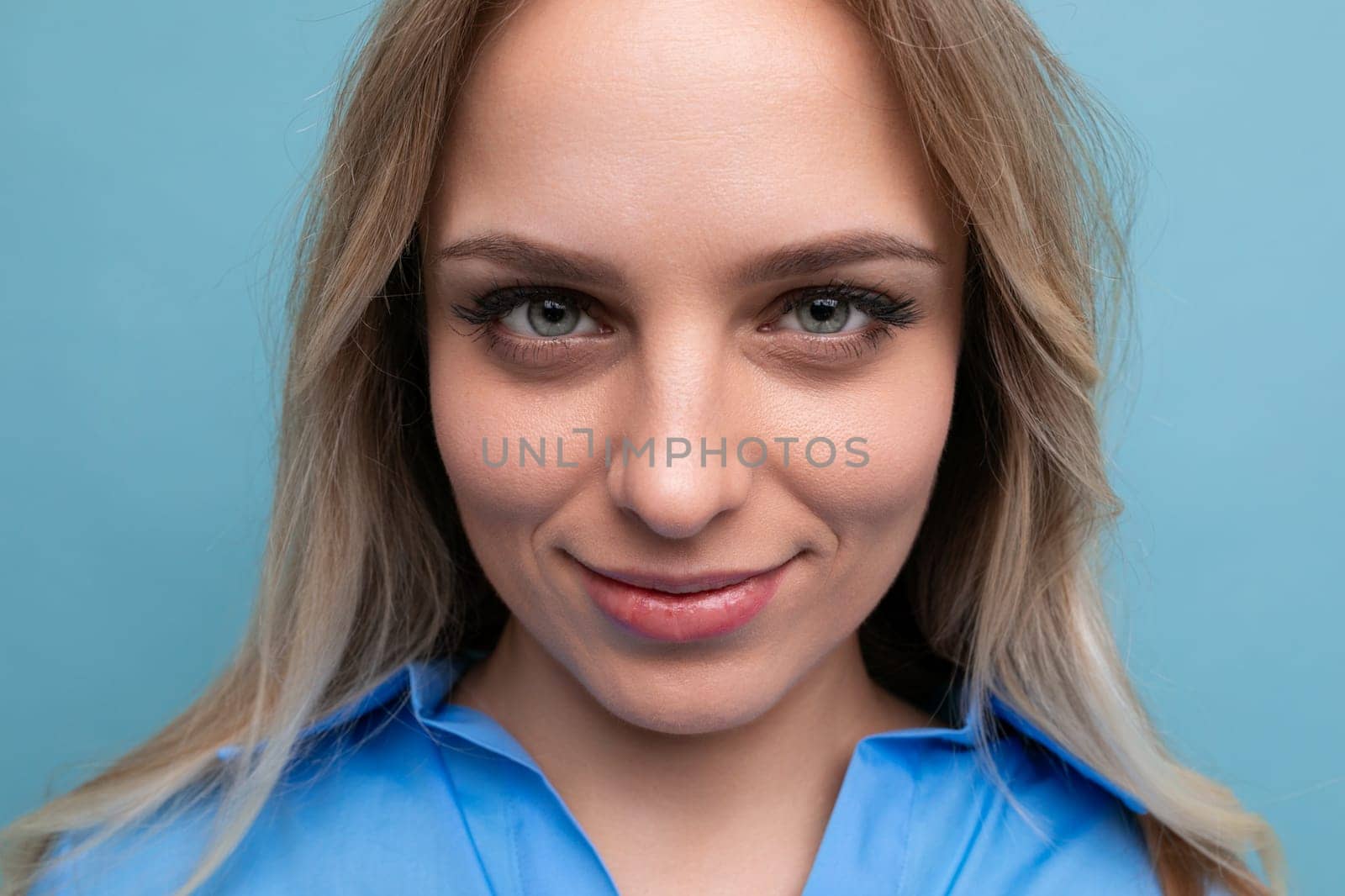 portrait of an adorable blonde young woman cutely closing her eyes on a blue background.
