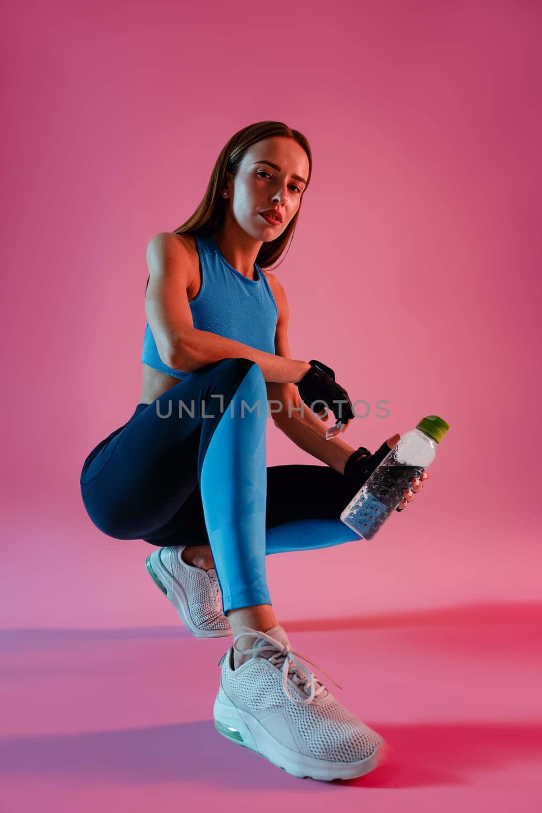Fitness healthy woman sitting with water bottle in sport clothing over studio background by Yaroslav_astakhov