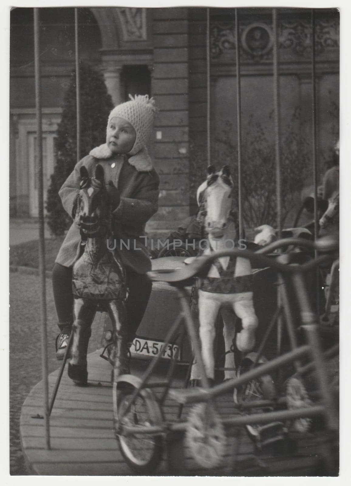 Vintage photo shows child at the amusement park. Child and merry-go-round. Retro black and white photography. Circa 1970s. by roman_nerud