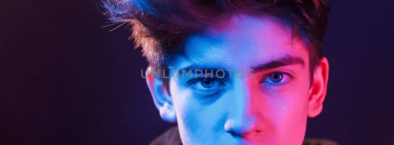 Portrait of young beautiful guy with fashionable haircut. Neon lighting.