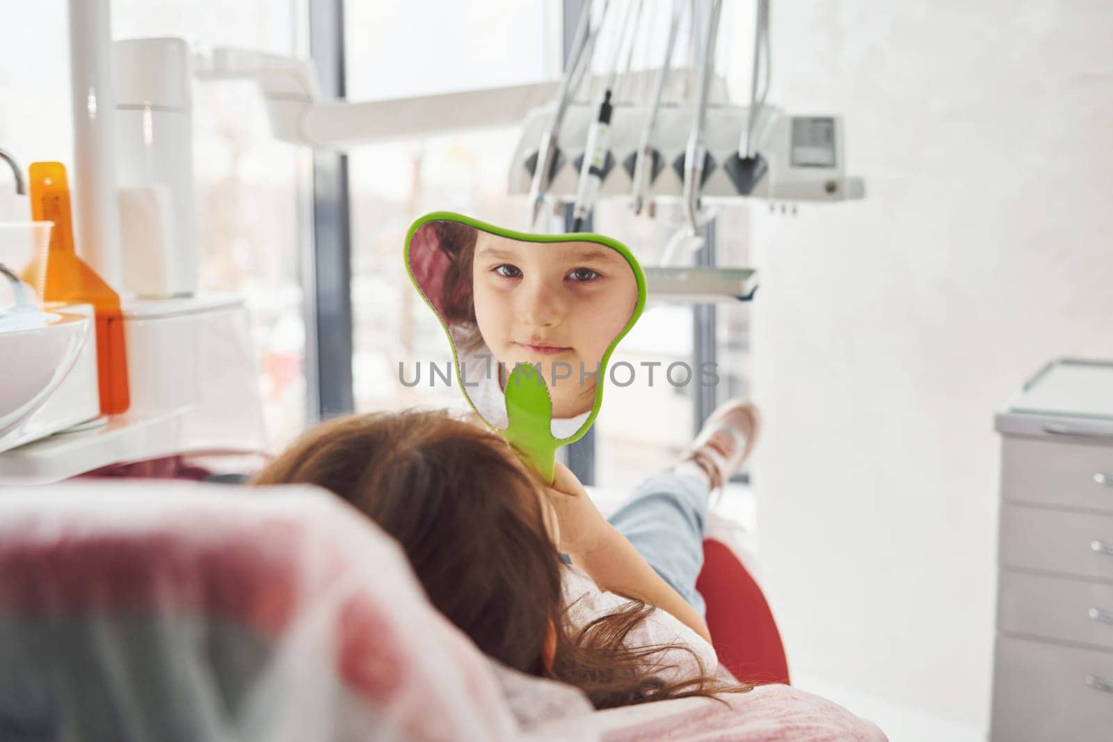 Looks into the mirror. Little girl visiting dentist in clinic. Conception of stomatology.