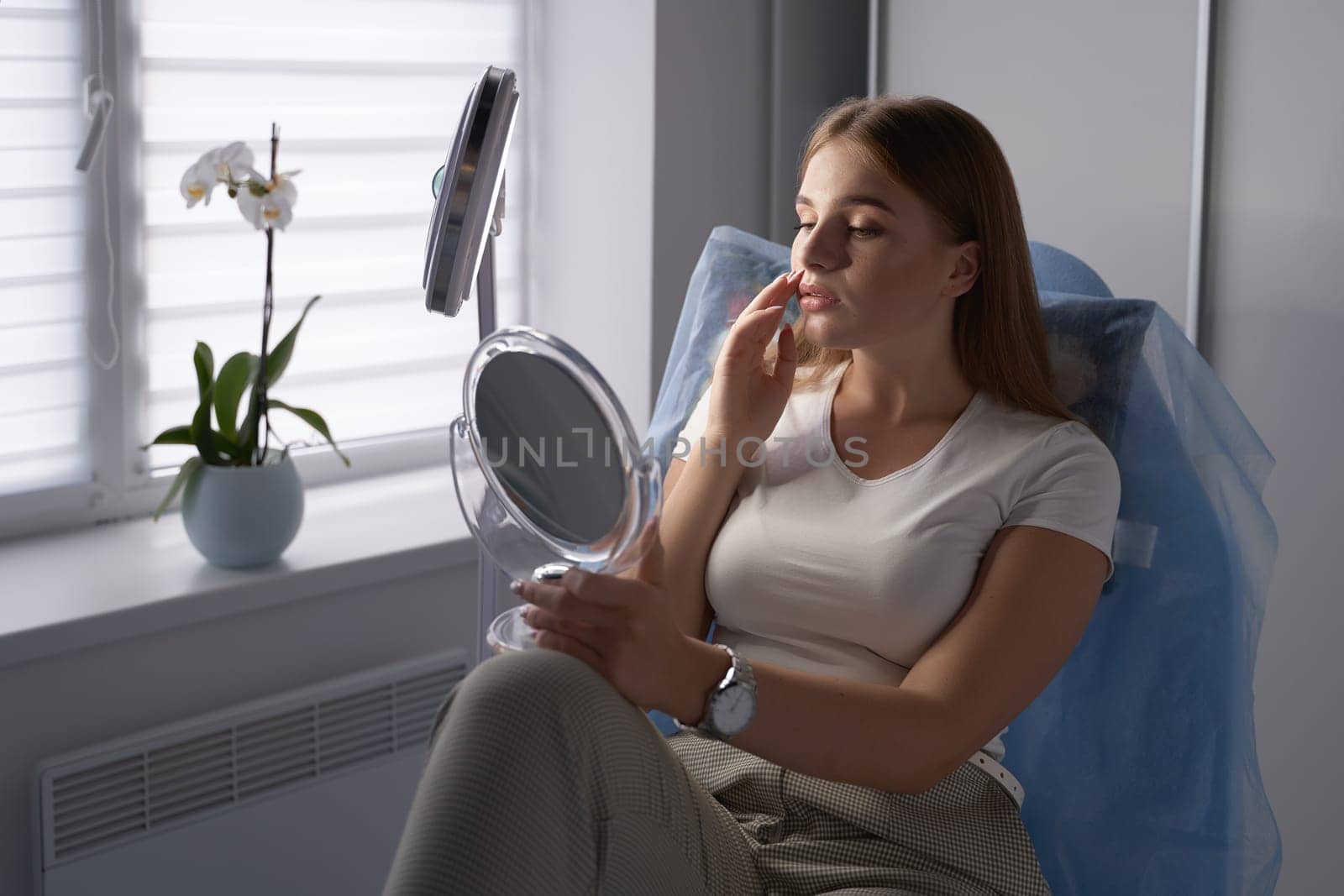 Young beautiful female customer with mirror getting ready for beauty procedures in a medical salon