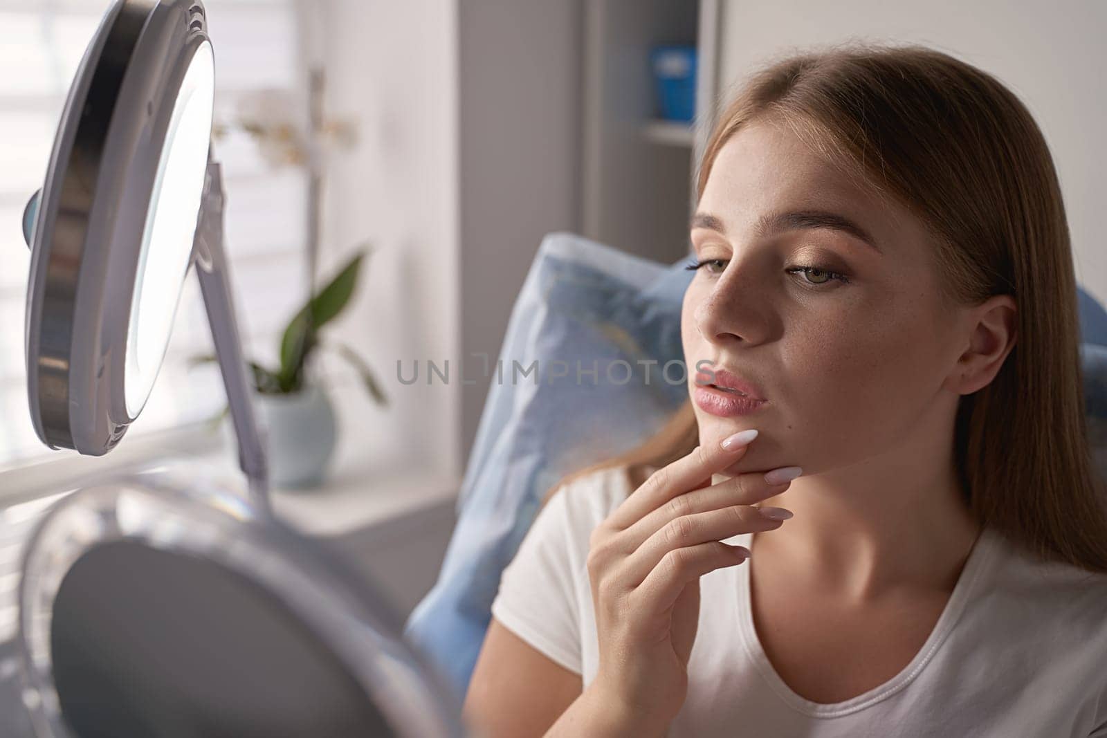 Young beautiful female customer with mirror getting ready for beauty procedures in a medical salon
