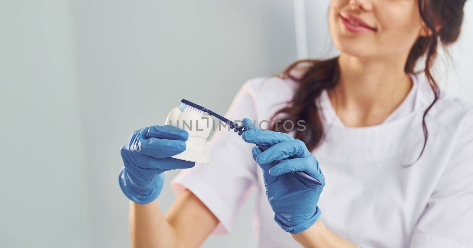 Brush and tooth. Portrait of professional female dentist with equipment that standing indoors.