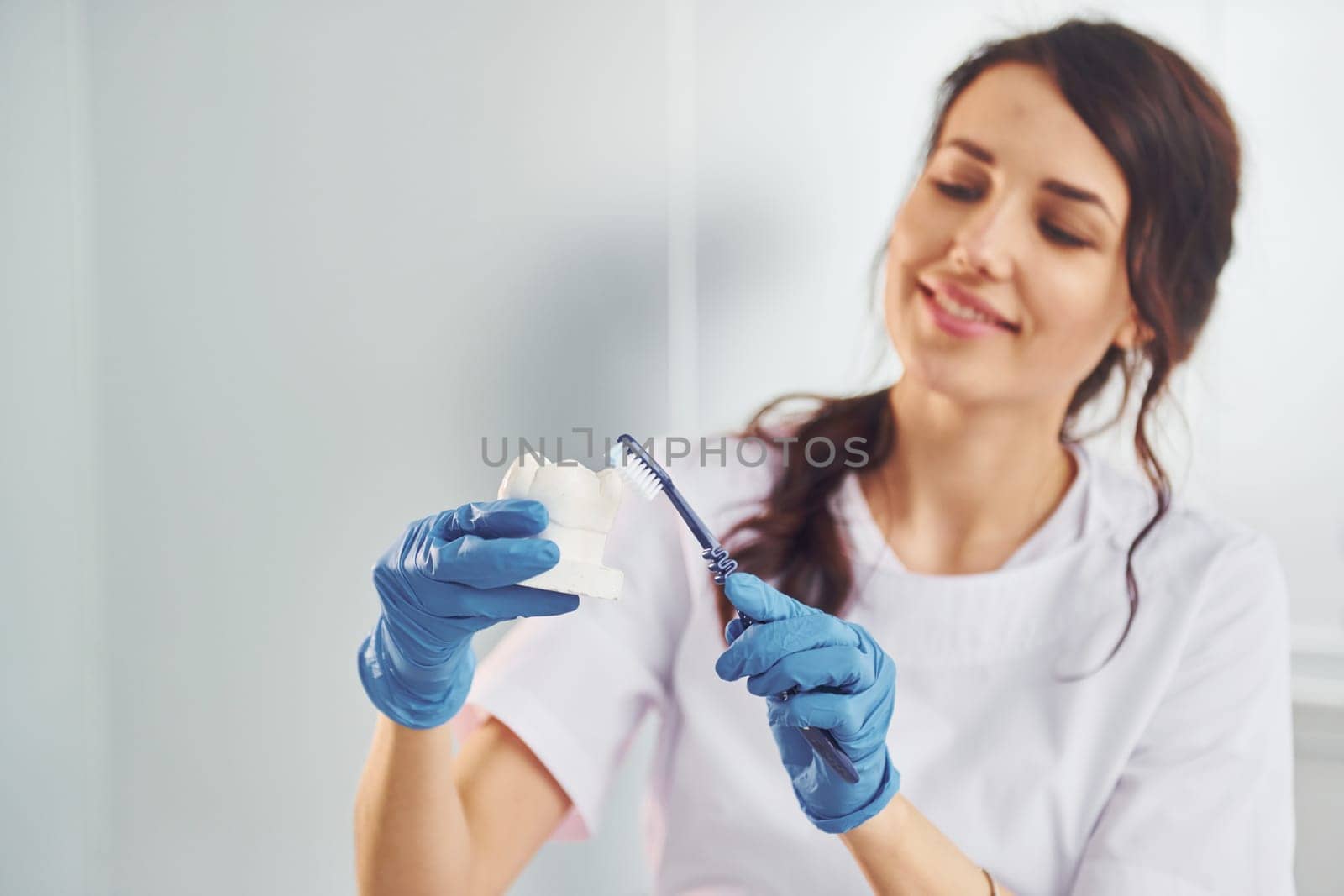 Brush and tooth. Portrait of professional female dentist with equipment that standing indoors by Standret