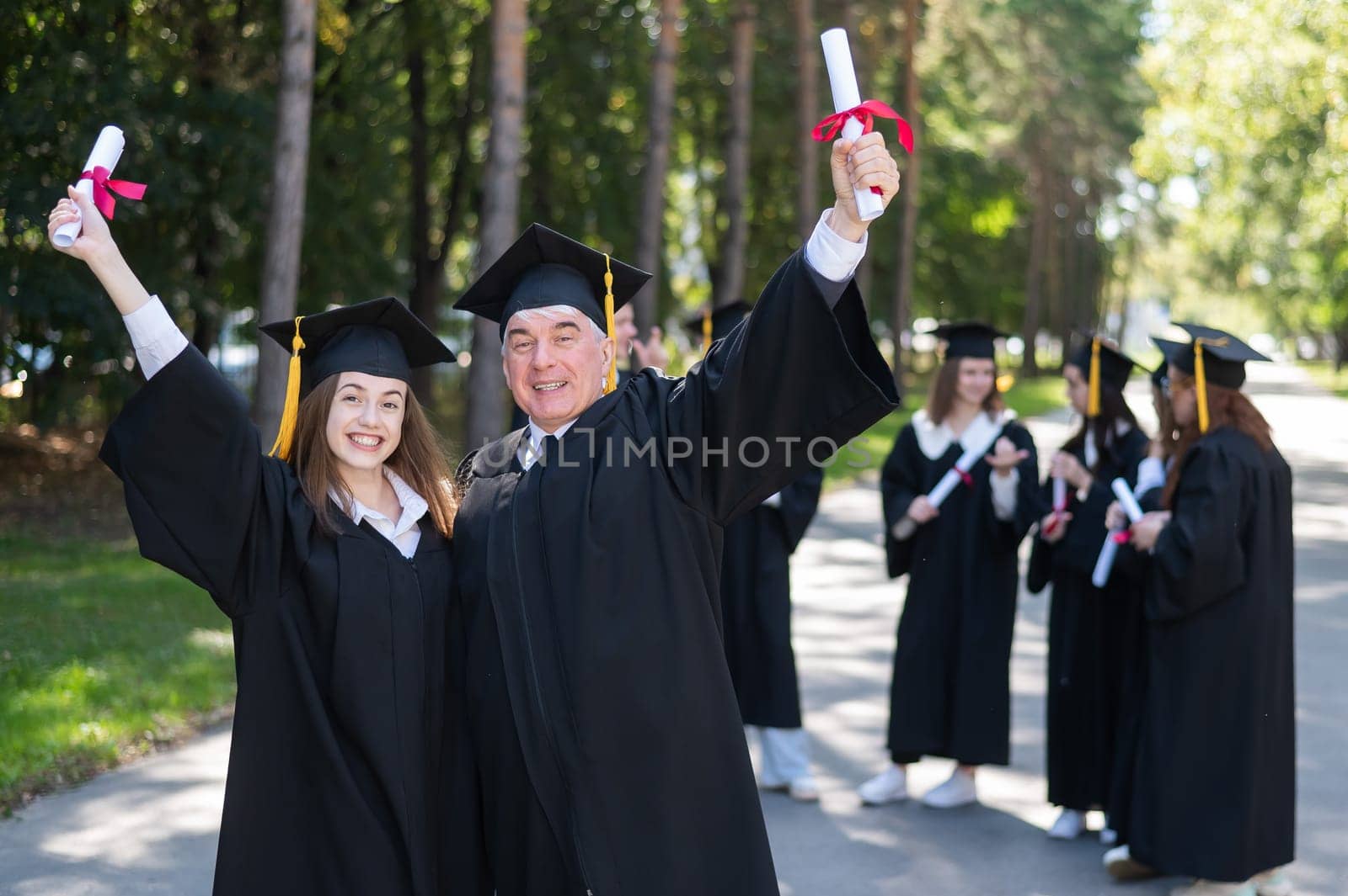 A group of graduates in robes outdoors. An elderly man and a young woman congratulate each other on their graduation. by mrwed54