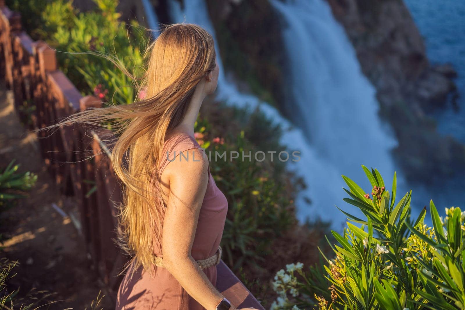 Beautiful woman with long hair on the background of Duden waterfall in Antalya. Famous places of Turkey. Lower Duden Falls drop off a rocky cliff falling from about 40 m into the Mediterranean Sea in amazing water clouds. Tourism and travel destination photo in Antalya, Turkey. Turkiye.