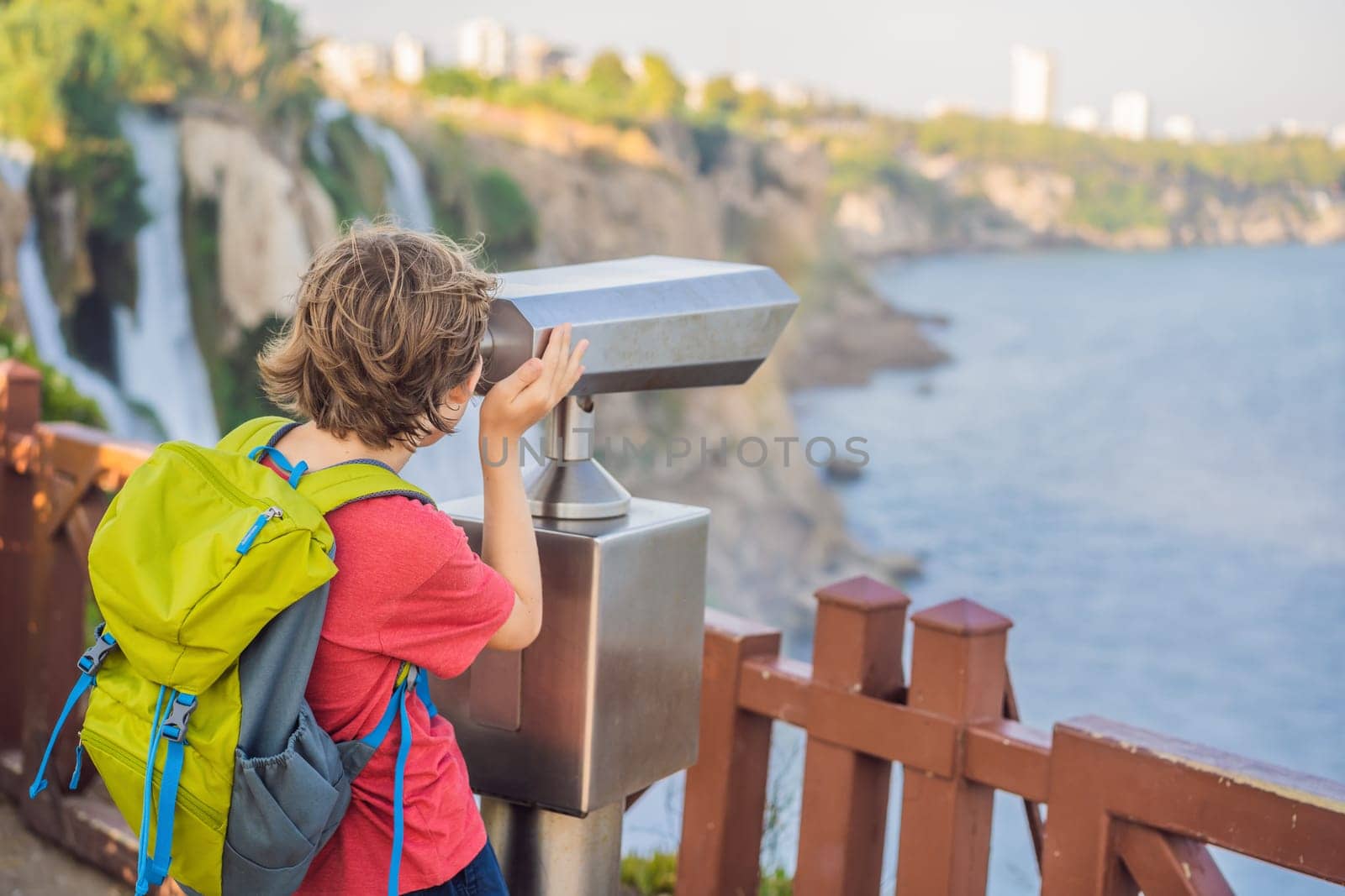 Boy tourist with a backpack on the background of Duden waterfall in Antalya. Famous places of Turkey. Lower Duden Falls drop off a rocky cliff falling from about 40 m into the Mediterranean Sea in amazing water clouds. Tourism and travel destination photo in Antalya, Turkey. Turkiye.
