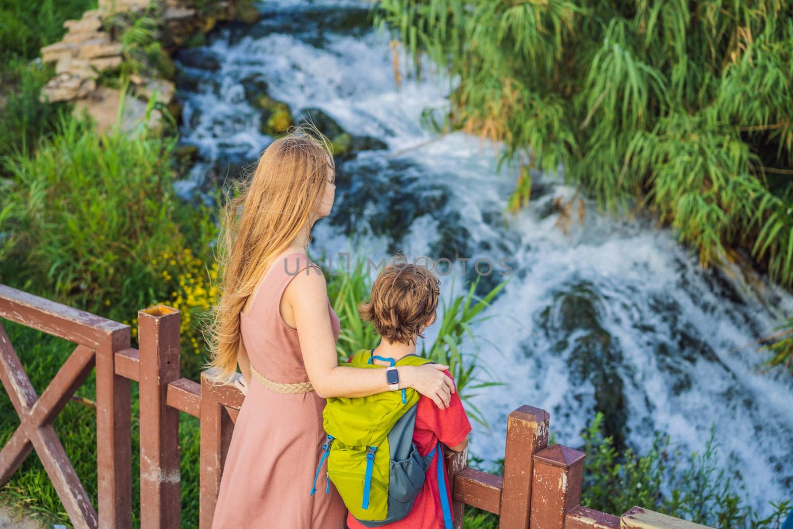 Mother and son tourists on the background of Duden waterfall in Antalya. Famous places of Turkey. Lower Duden Falls drop off a rocky cliff falling from about 40 m into the Mediterranean Sea in amazing water clouds. Tourism and travel destination photo in Antalya, Turkey. Turkiye.
