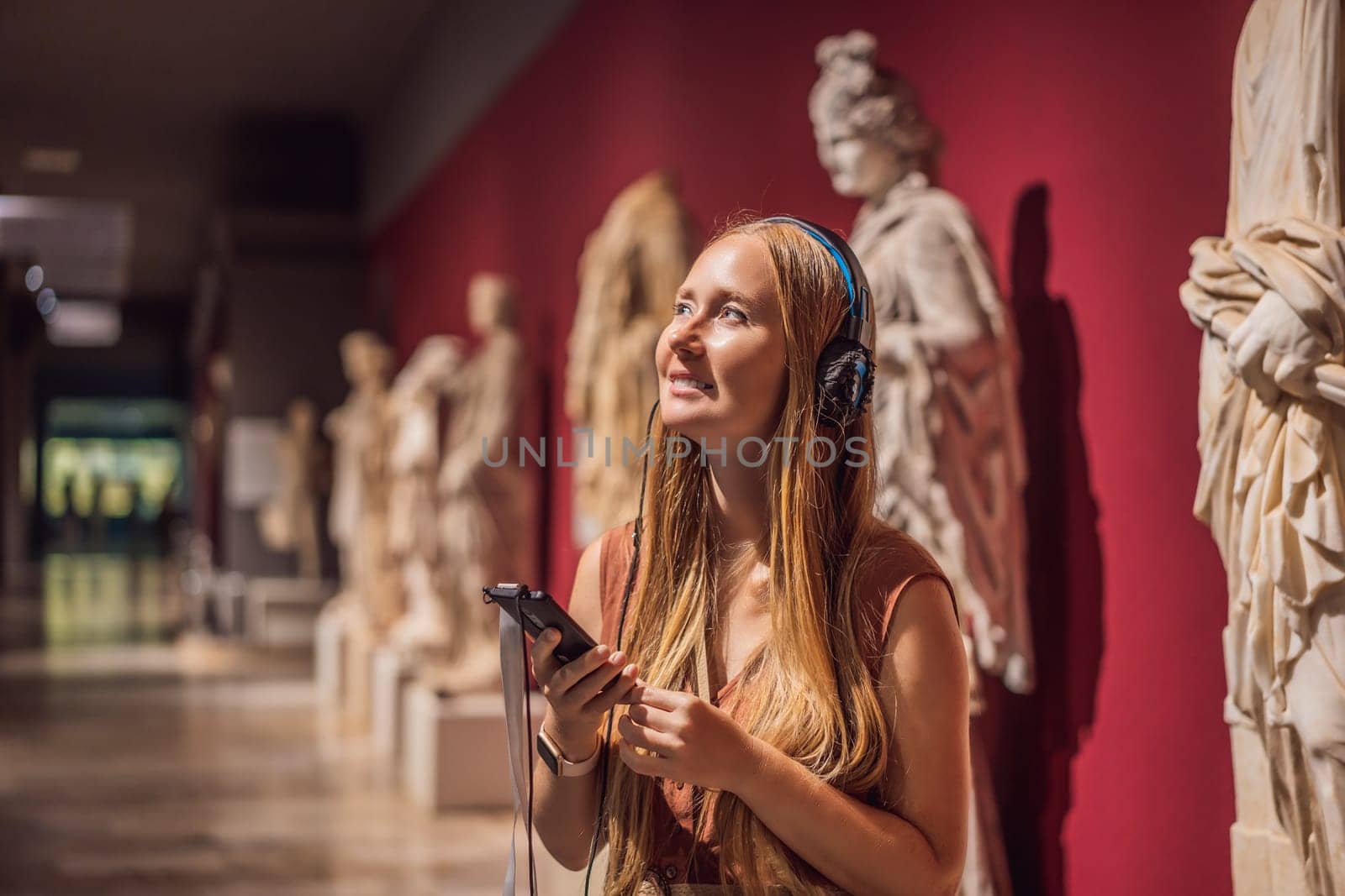 Portrait of contemporary young woman looking at sculptures and listening to audio guide at museum exhibition.
