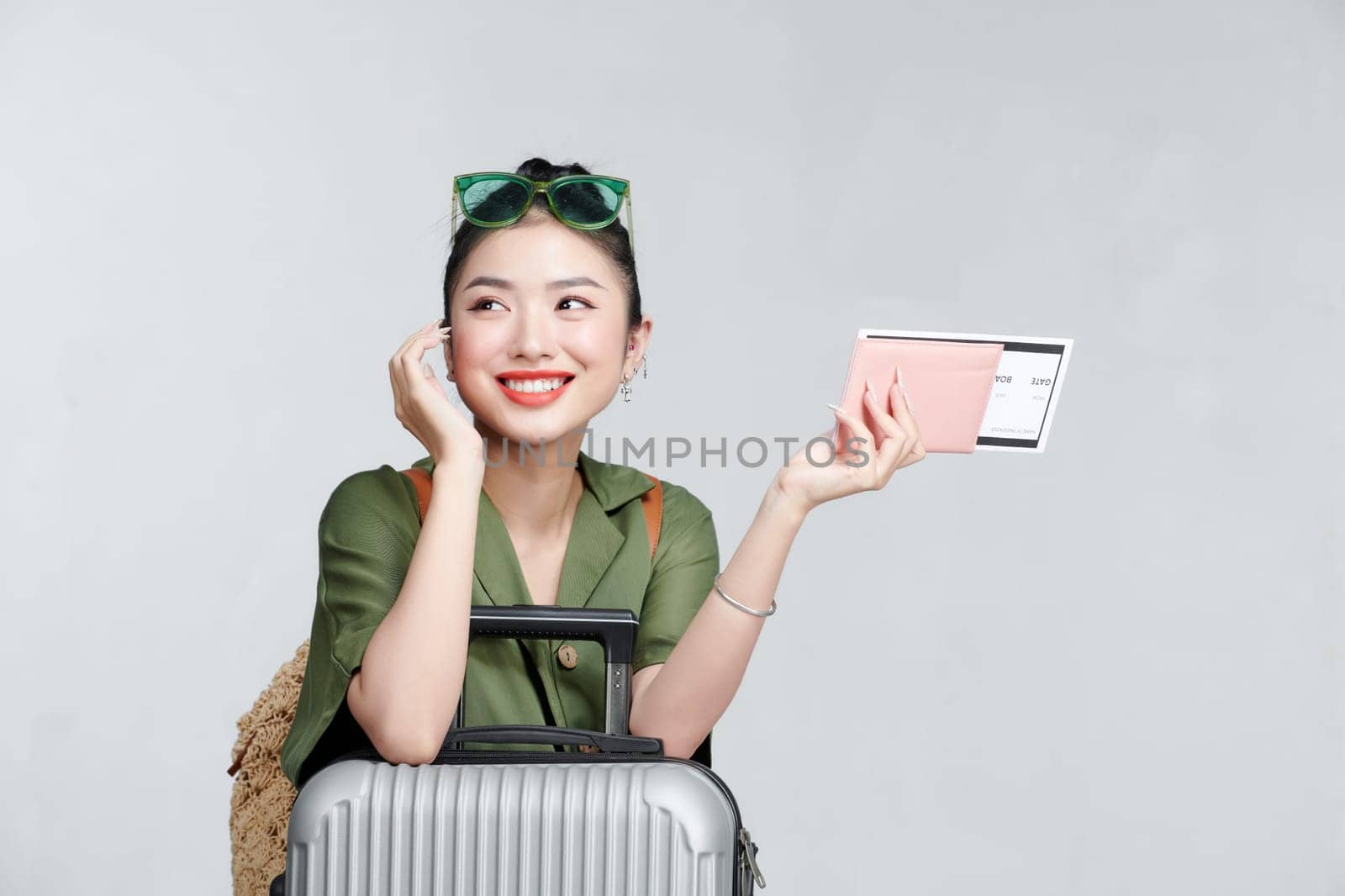 Enthusiastic asian girl shows passport tickets, smiling pleased, standing with suitcase, gray background by makidotvn