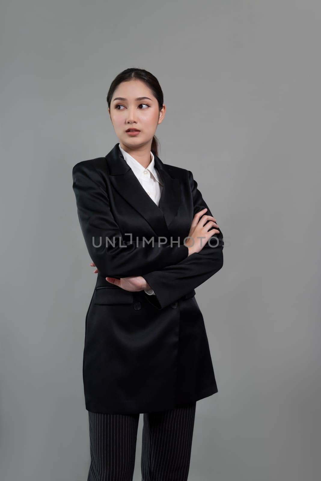 Confident young businesswoman stands on isolated background, posing in formal black suit. Office lady or manager with smart and professional appearance. Enthusiastic