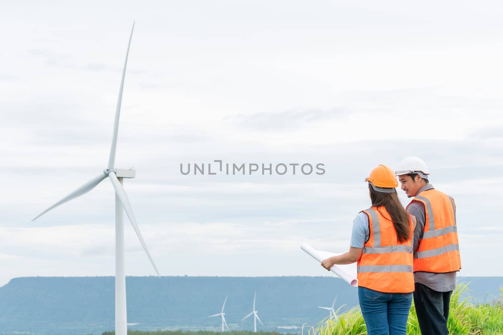 Male and female engineers working on a wind farm atop a hill or mountain in the rural. Progressive ideal for the future production of renewable, sustainable energy.