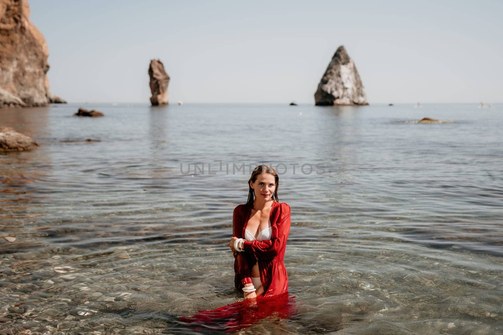 Woman travel sea. Happy tourist in red dress enjoy taking picture outdoors for memories. Woman traveler posing in sea beach, surrounded by volcanic mountains, sharing travel adventure journey by panophotograph