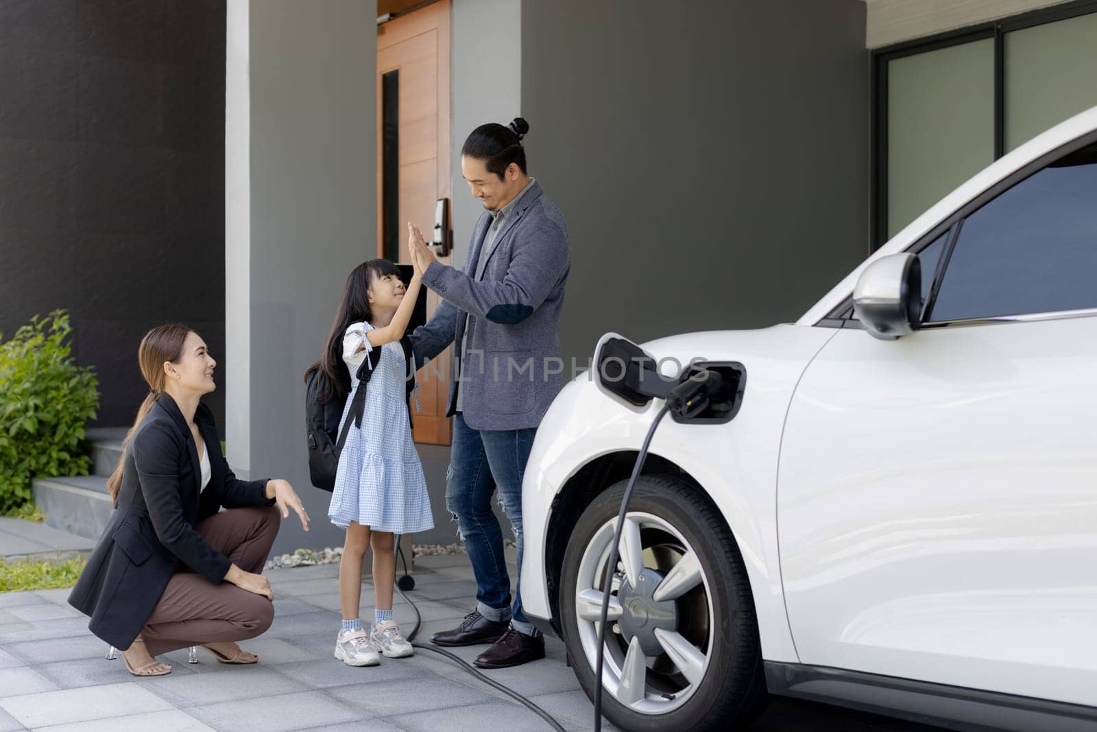 Progressive young parents and daughter living in a home with an electric car. by biancoblue