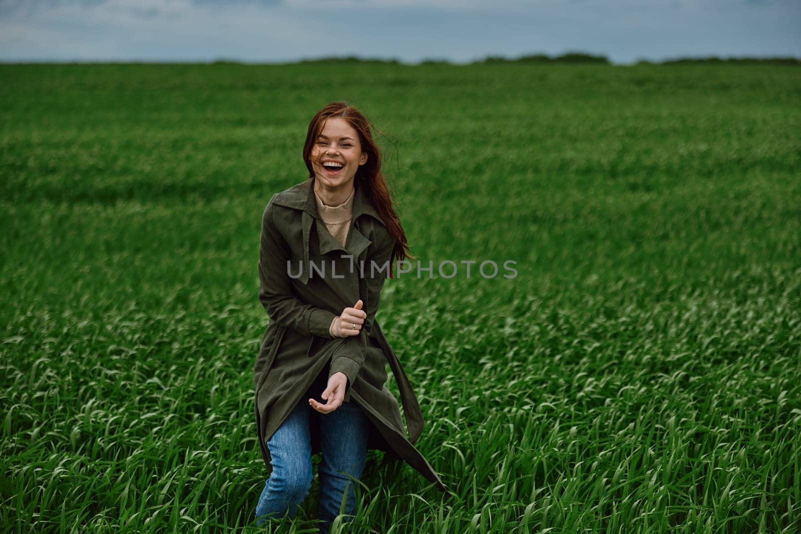 red-haired, happy woman stands in a green field in rainy weather. Emotions, harmony with nature. High quality photo