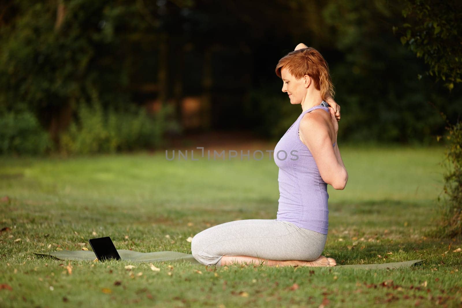 Getting some online yoga tips. an attractive woman doing yoga at the park with her tablet beside her. by YuriArcurs