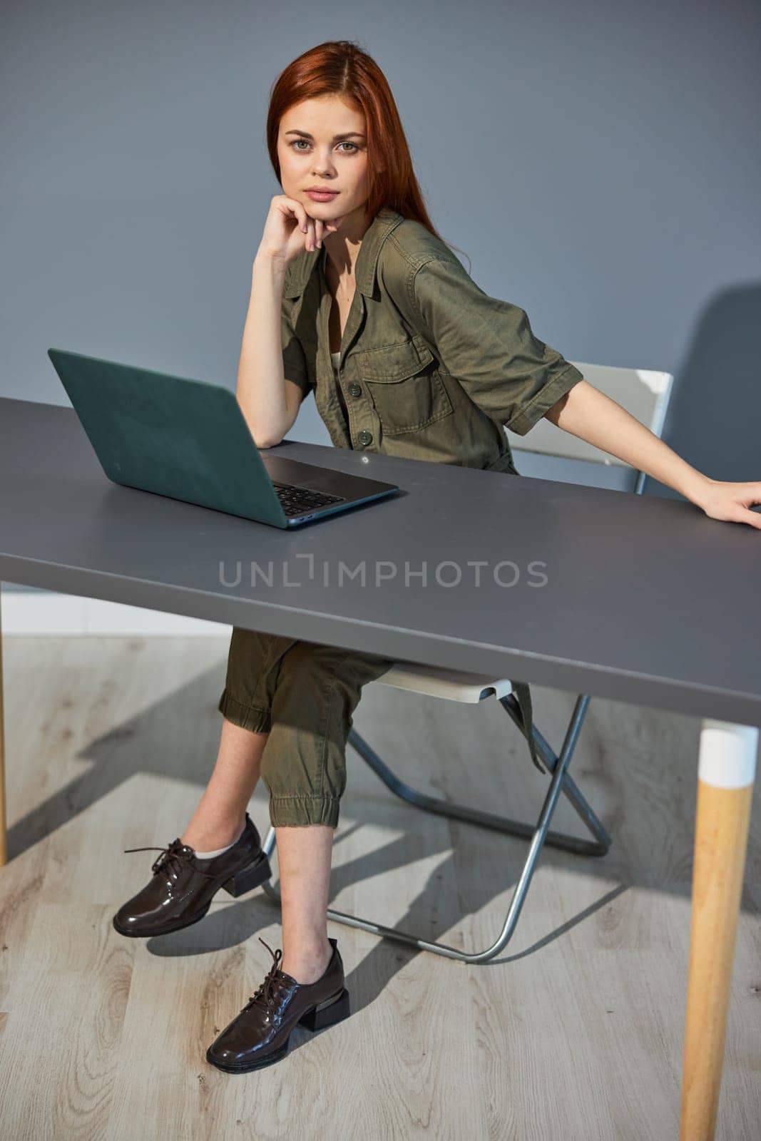 photo of a woman sitting at a table with a laptop in the office against the background of a blue wall. High quality photo