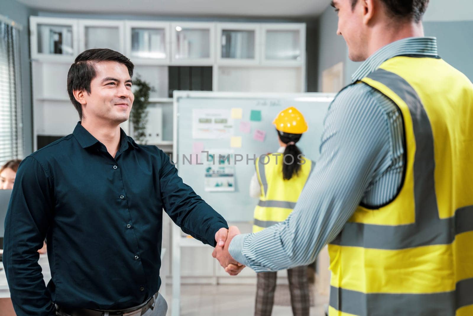 An engineer with a protective vest handshake with an investor in his office by biancoblue