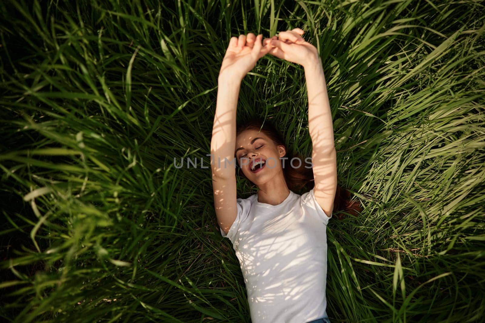 happy woman lies in high grass lit by the sun stretching her hands to the camera by Vichizh