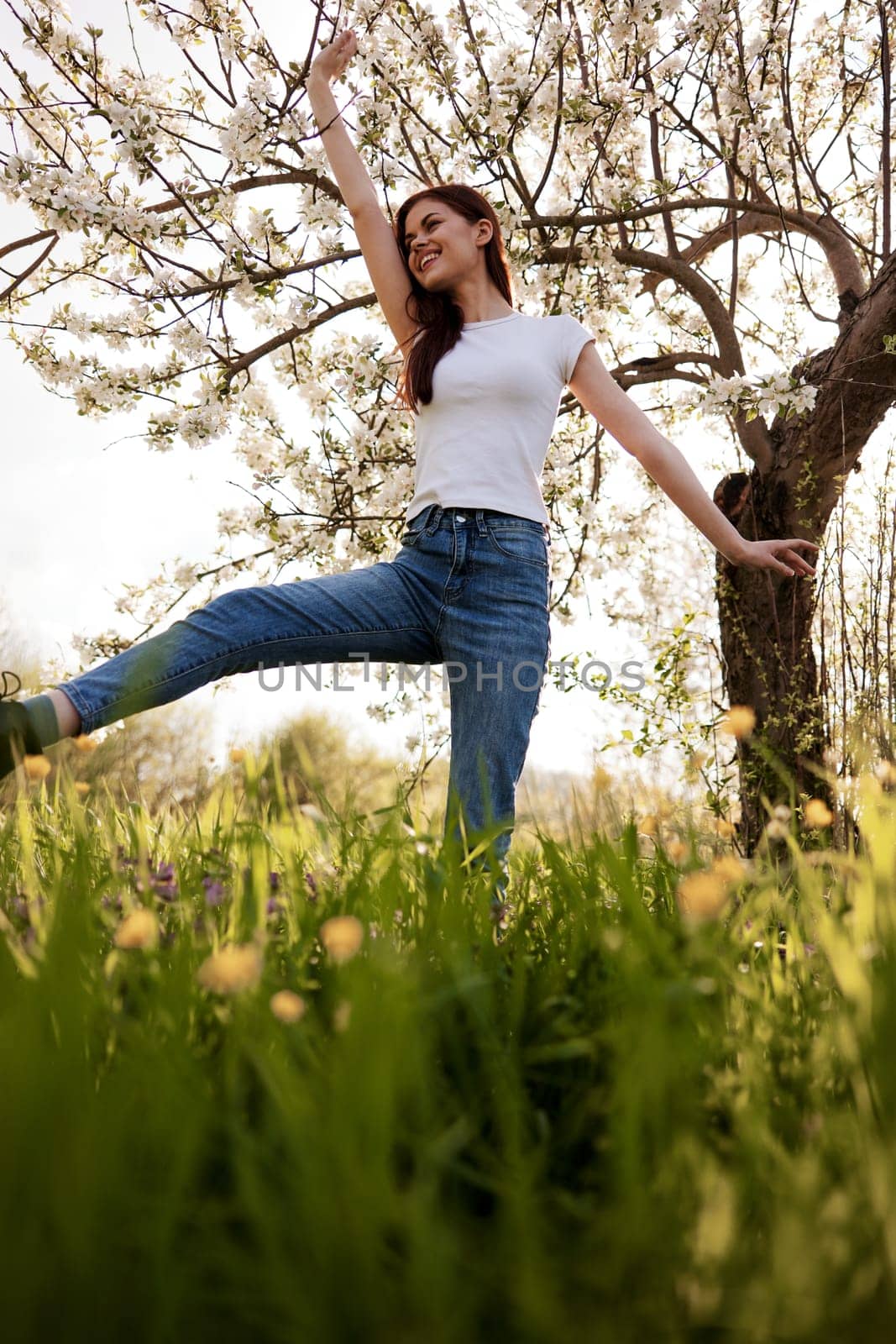 active woman posing raising her leg up against the background of a flowering tree in the park by Vichizh