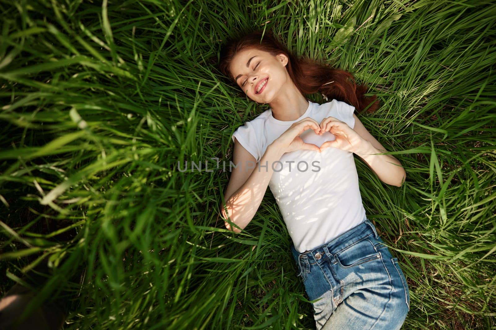 happy woman folded her arms on her chest in the shape of a heart lying in the grass. High quality photo