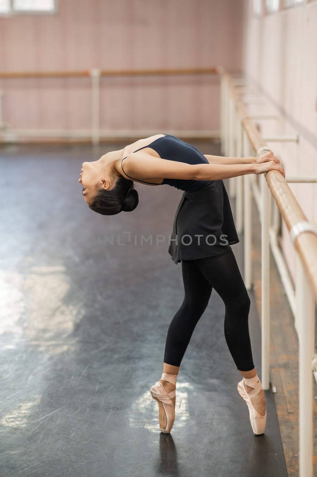 Asian woman doing back flexibility exercises at the ballet barre. by mrwed54