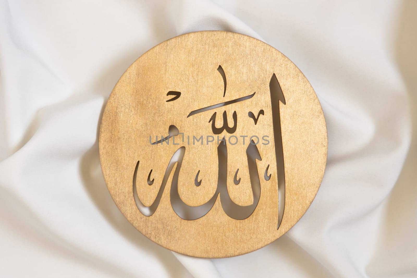 Allah bismillah names close up. Golden wooden calligraphy of islamic god. on white textile, top view. by Ri6ka