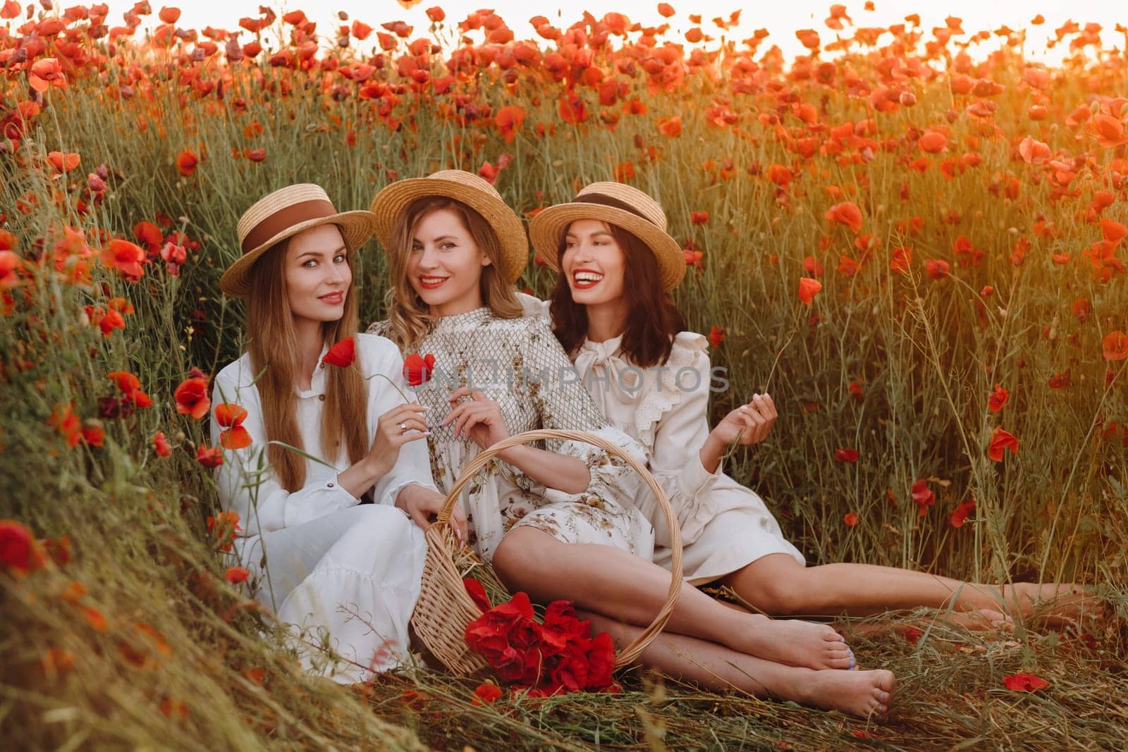 Funny girls in dresses and hats in a poppy field at sunset.