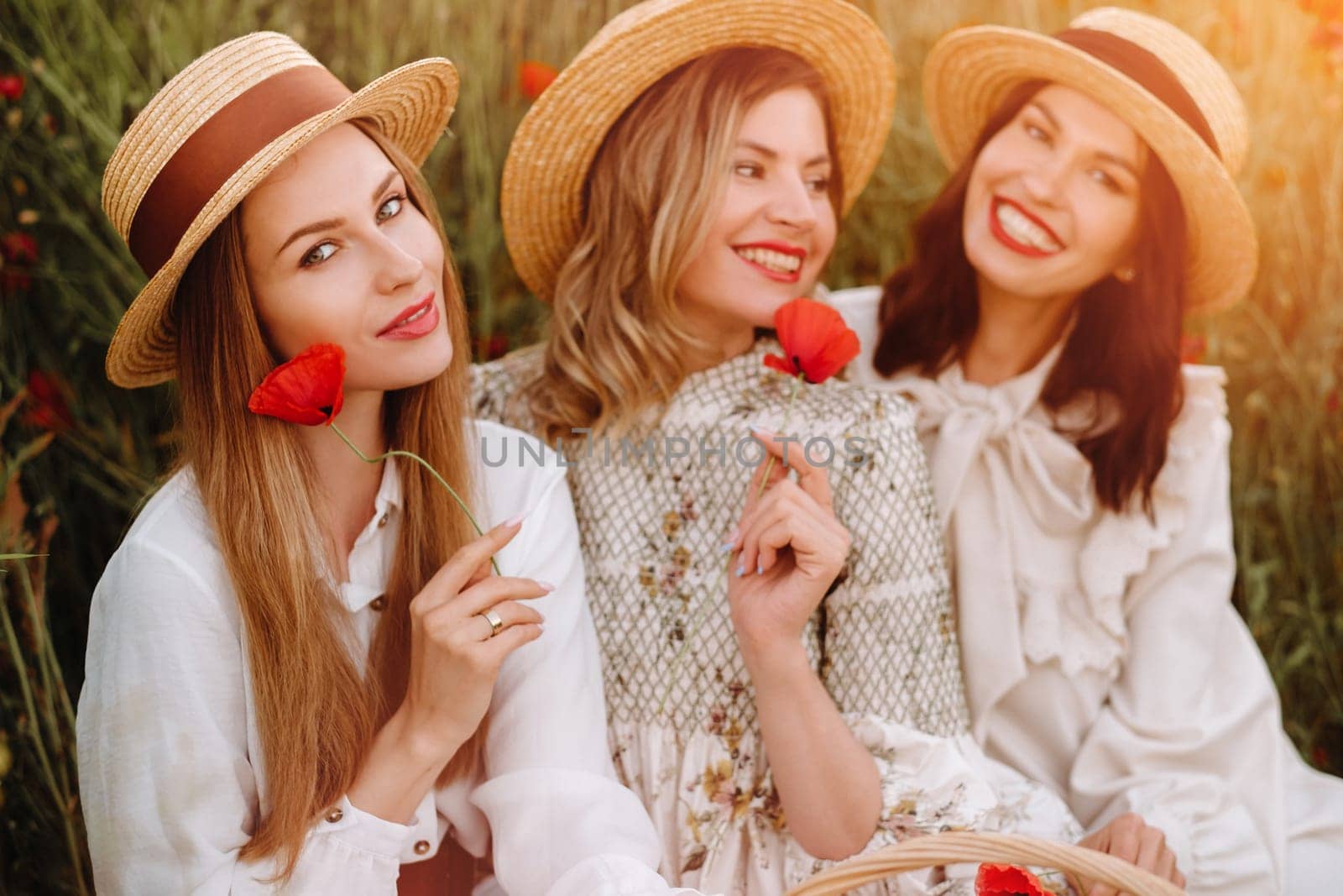 Funny girls in dresses and hats in a poppy field at sunset.