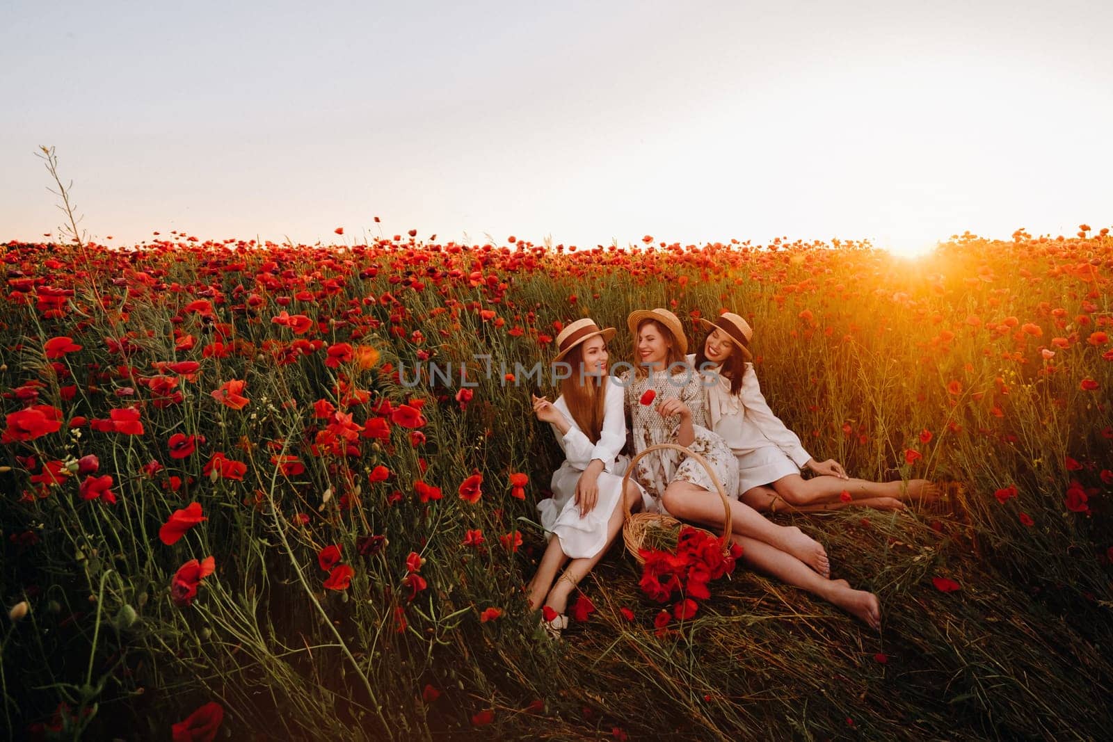 Funny girls in dresses and hats in a poppy field at sunset.