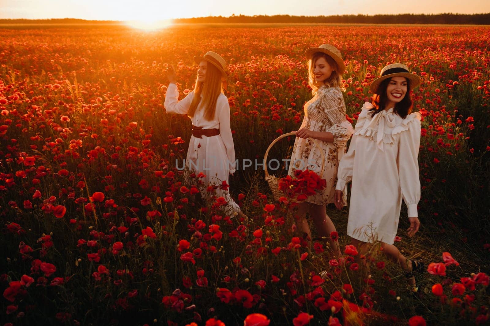 Funny girls in dresses and hats in a poppy field at sunset.