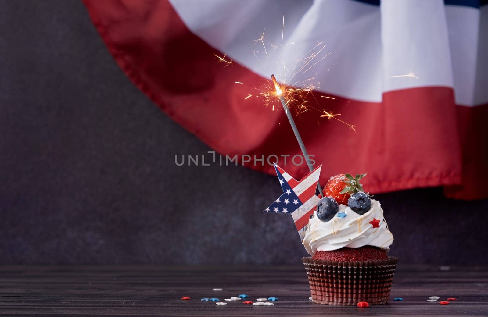 Fourth of july celebration. Sweet cupcake with blueberries and strawberry and sparkler over USA flag background