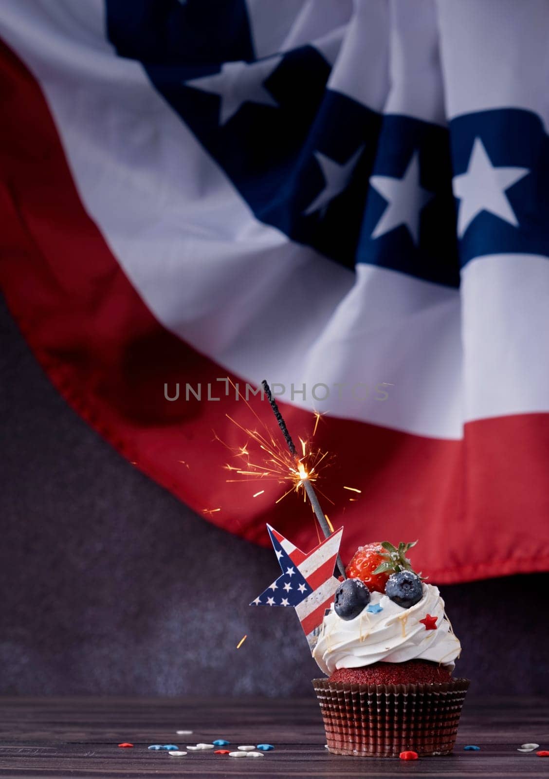 Fourth of july celebration. Sweet cupcake with blueberries and strawberry and sparkler over USA flag background